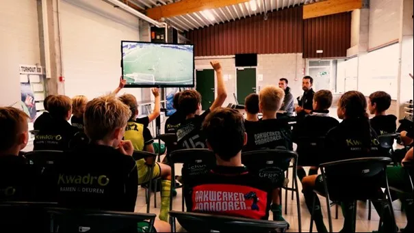 Voetballers die vragen stellen na het bekijken van beelden op het tactics board.